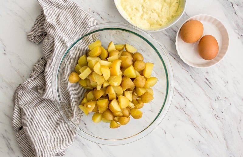 Bowl of diced Yukon potatoes and side bowl with eggs and yellow dressing.