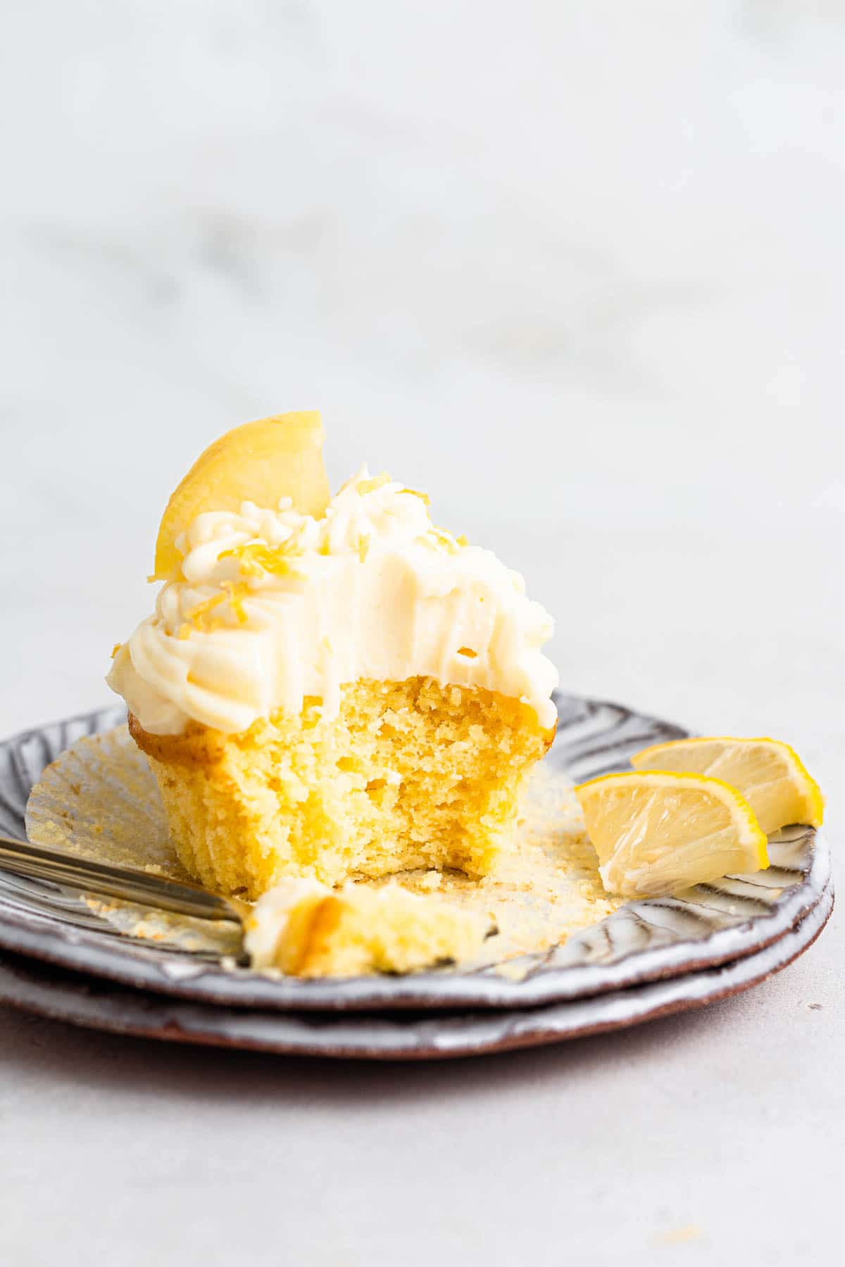 Single lemon cupcake with lemon cream cheese frosting on a plate.