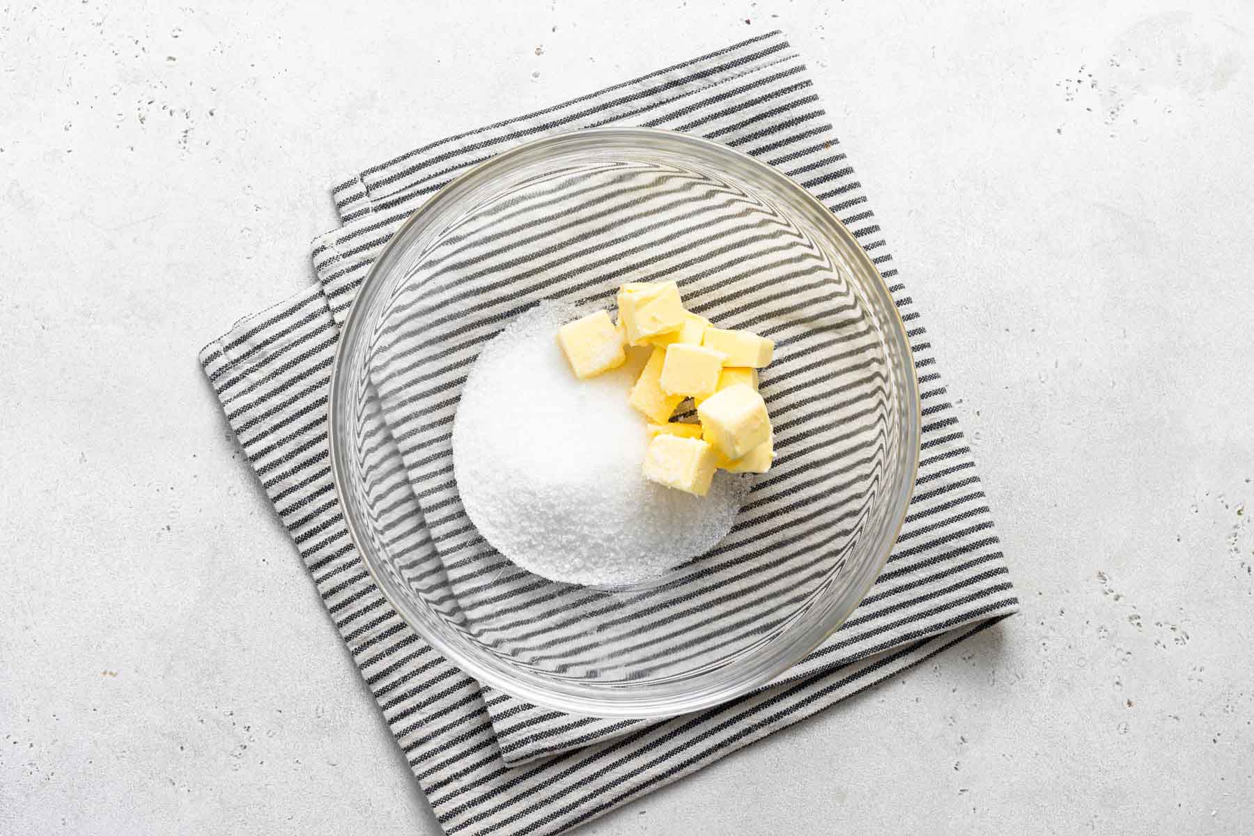 Diced butter and granulated sugar in clear glass bowl.