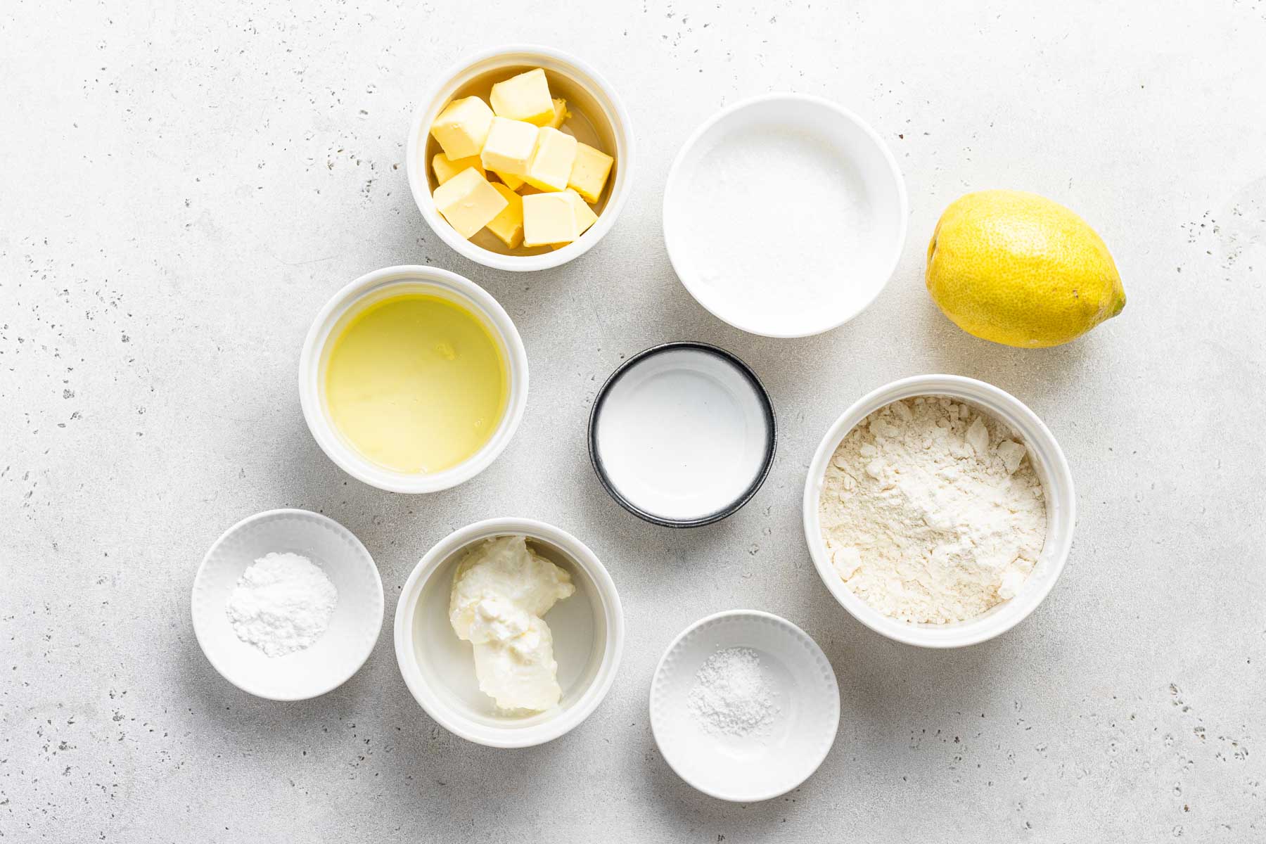 Ingredients for lemon cupcakes measured in white bowls.