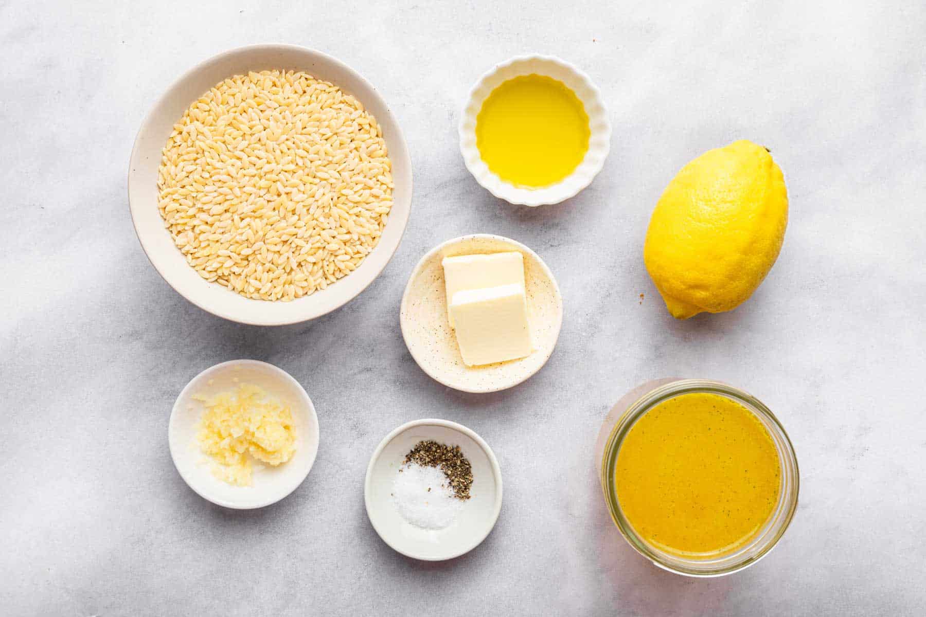 Bowl of pasta, oil, broth, lemon and butter on a grey table.