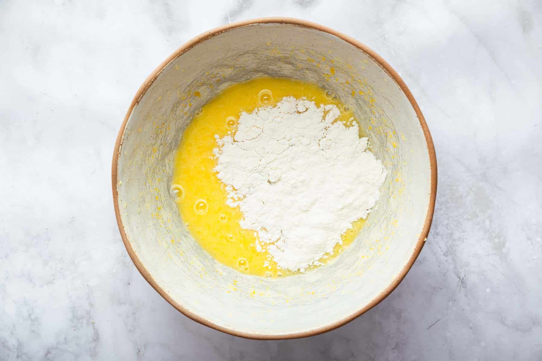 Bright yellow batter in bowl with white flour sprinkled evenly on top.