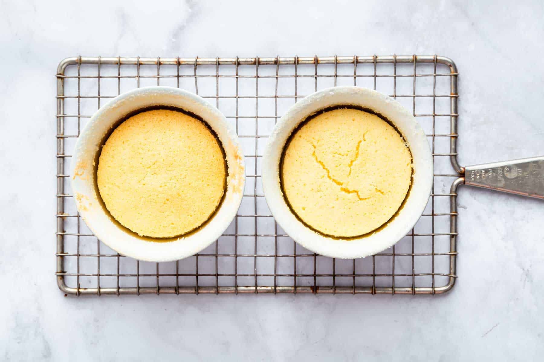 Two yellow cakes in ramekins cooling on a wire rack.
