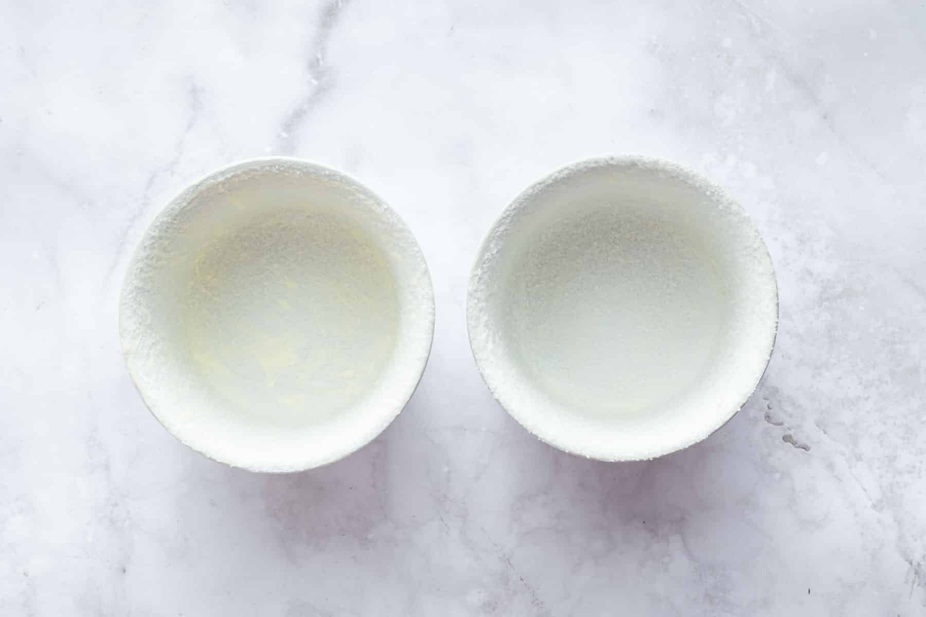 Two empty ramekins with butter and sugar on the insides.