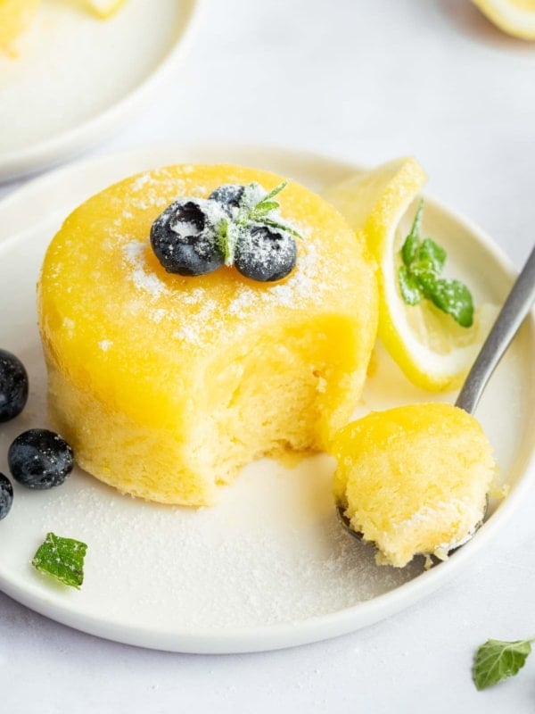 Bright yellow lemon pudding cake on a plate garnished with blueberries.