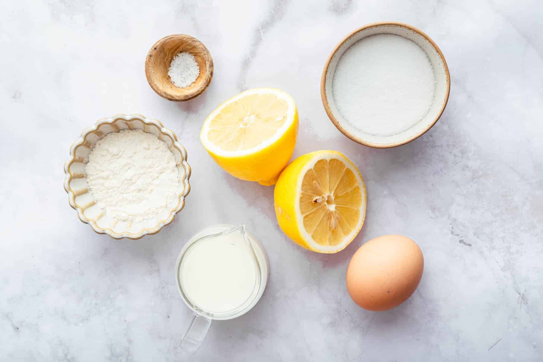 White bowls of flour, sugar, and milk on marble counter.