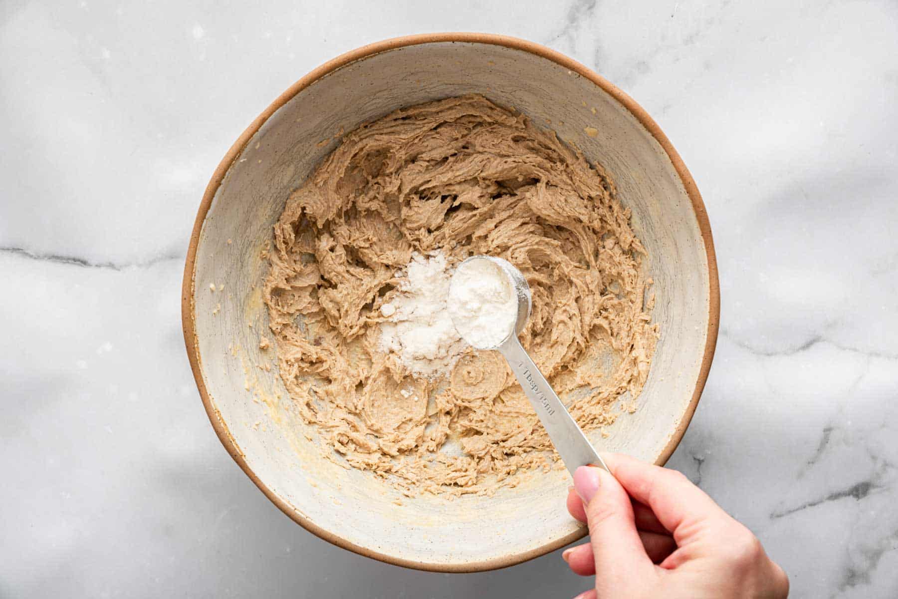 Hand adding tablespoonfuls of flour to a light brown dough.