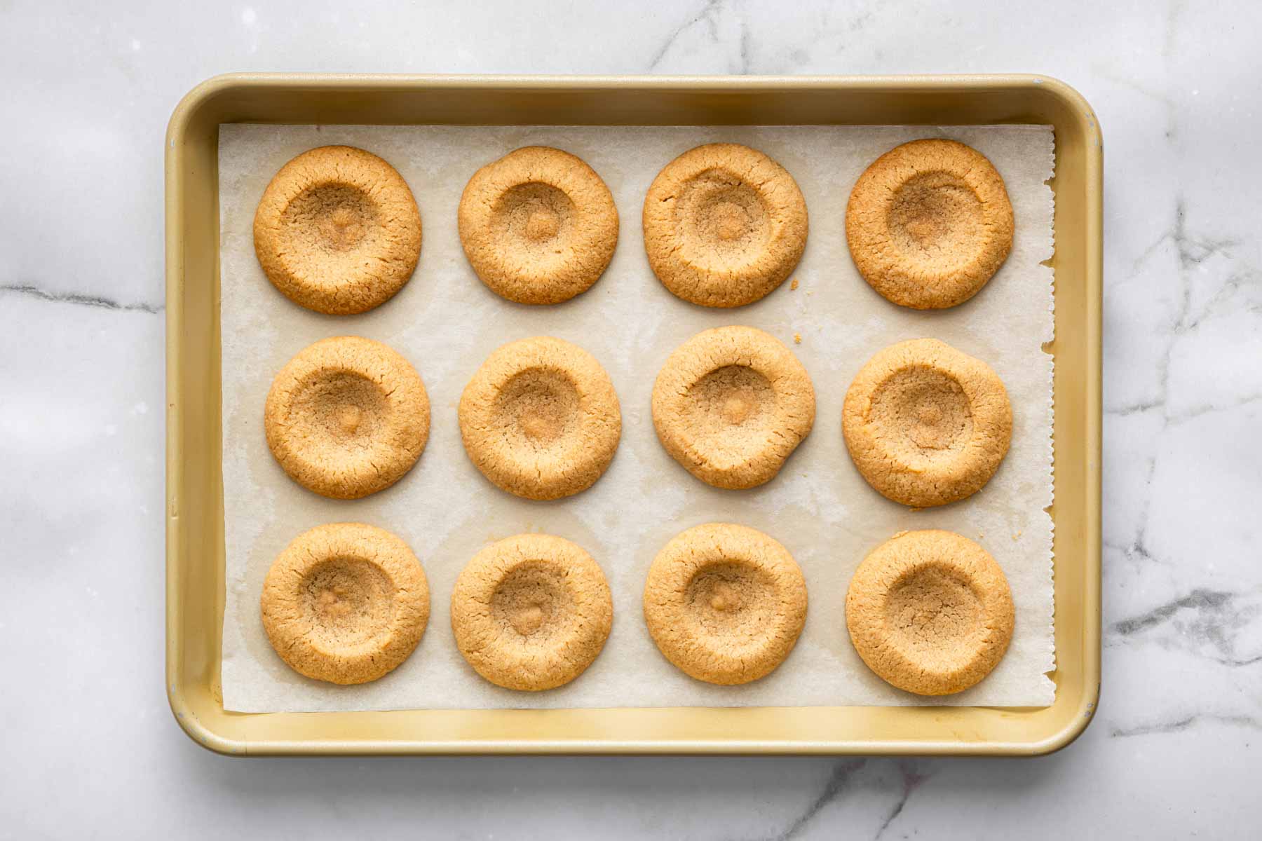 Freshly baked thumbprint cookies without any filling on a baking sheet.