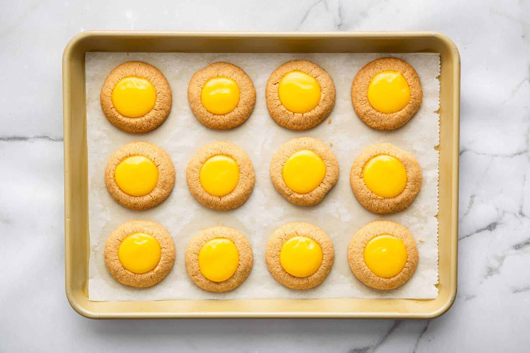 Bright yellow lemon thumbprint cookies on a baking sheet.