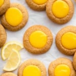 Bright yellow lemon thumbprint cookies on parchment paper.