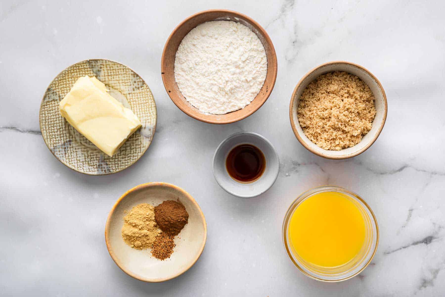 Pottery bowls with spices, butter, flour, and sugar on marble counter.