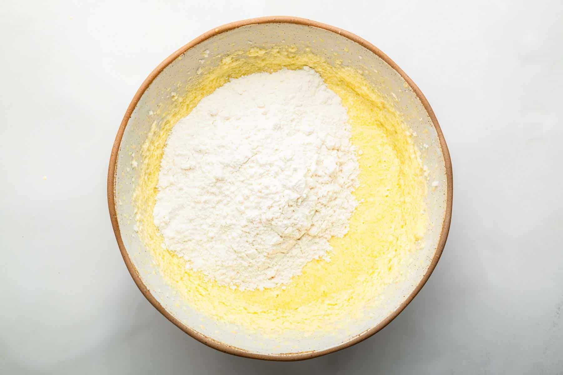 Flour sprinkled over yellow batter in shallow bowl.