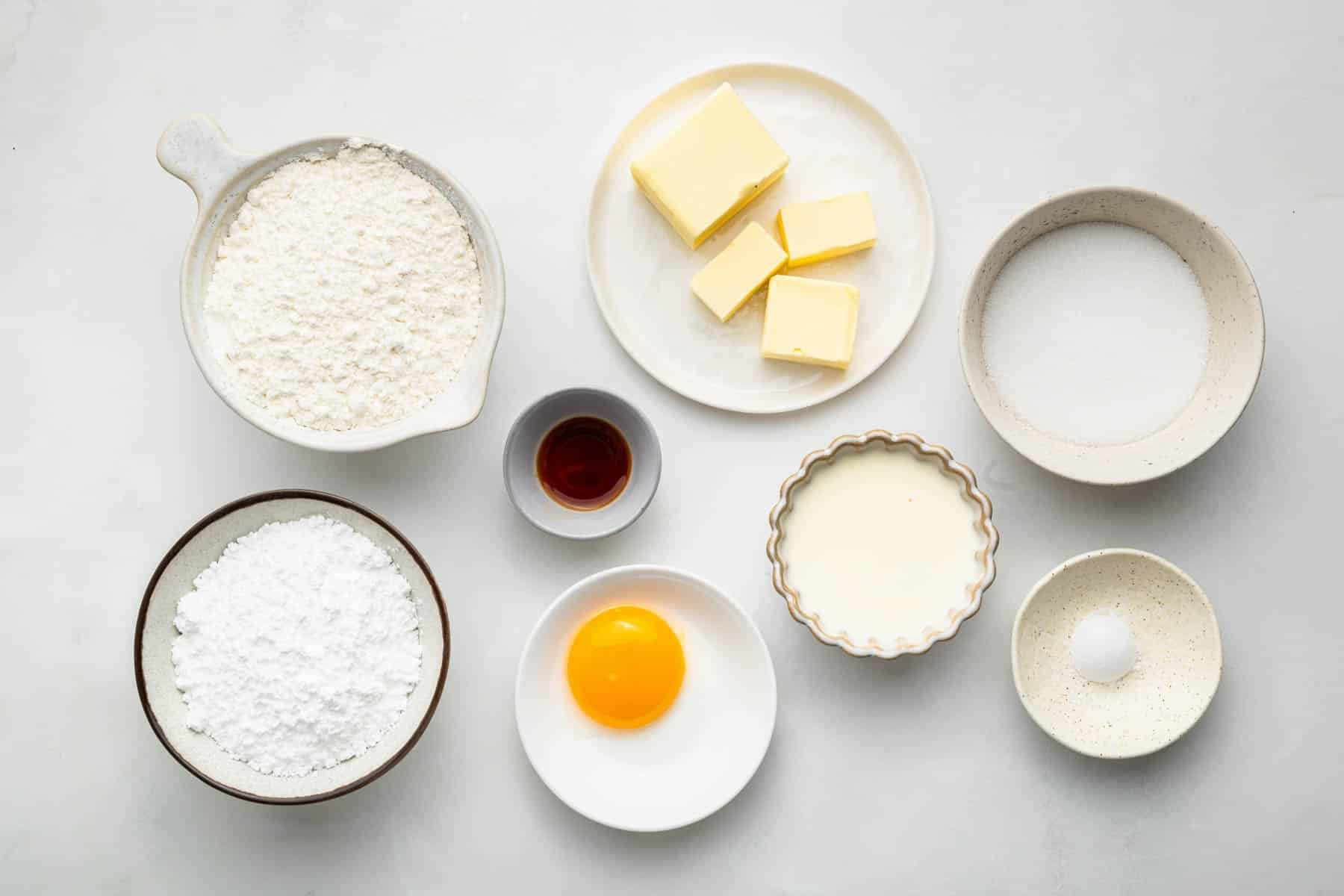 Small bowls of butter, egg yolk, vanilla, and baking ingredients.