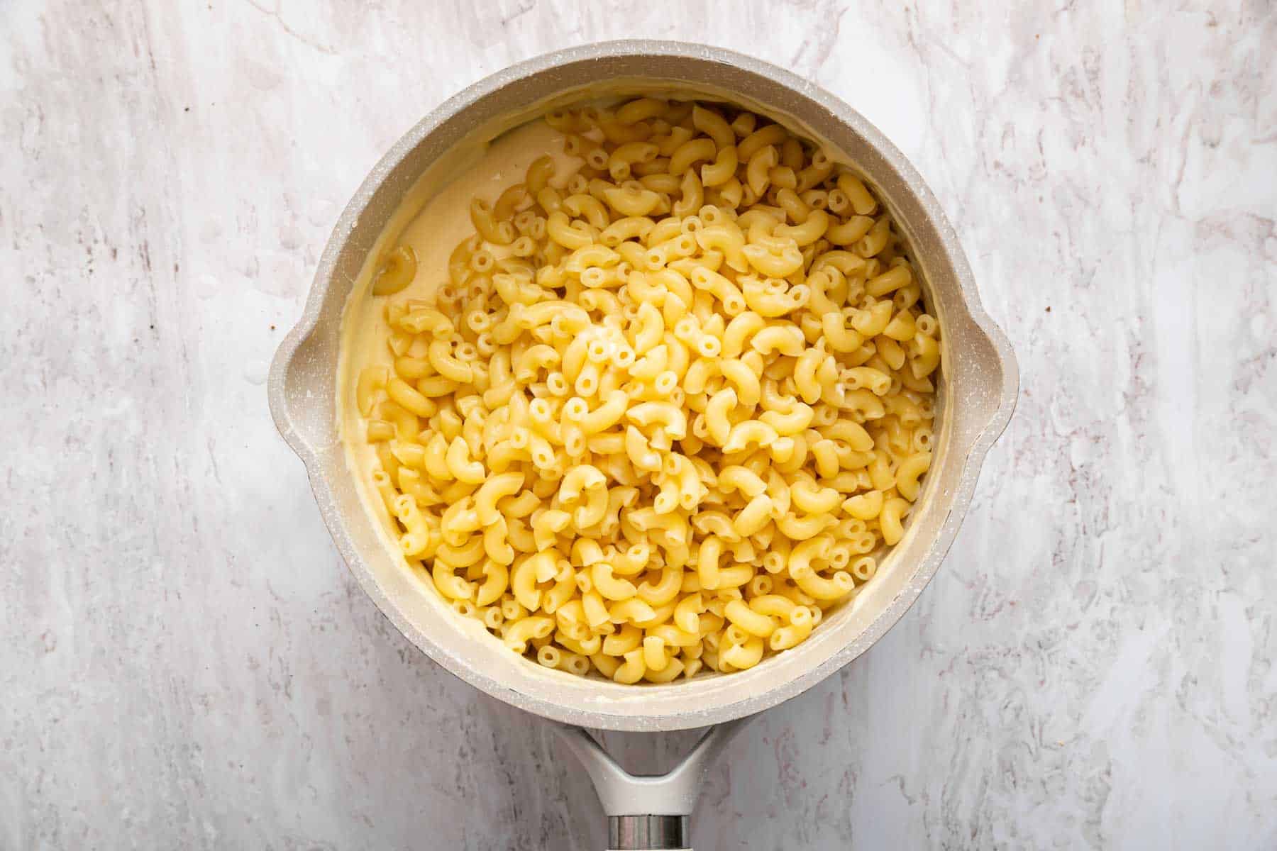 Freshly cooked pasta over a sauce in a small saucepan.