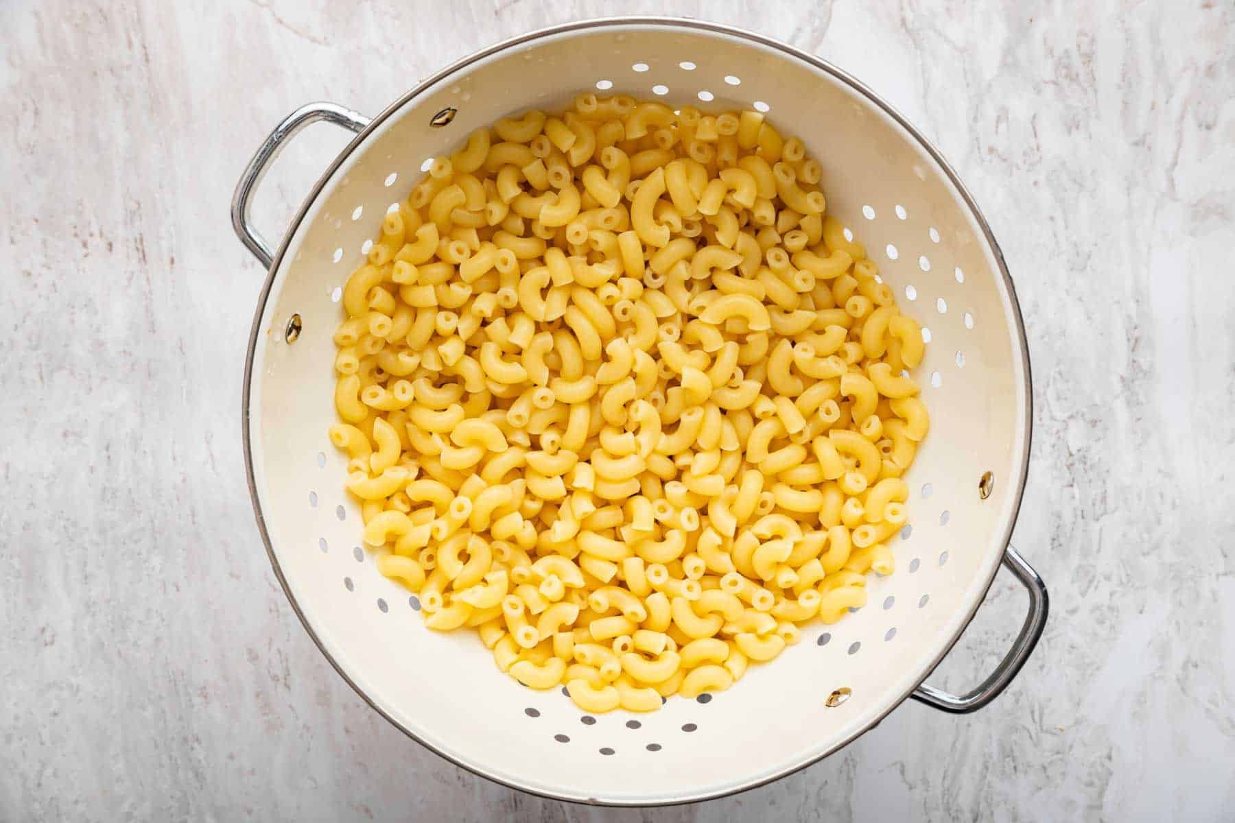 Fresh cooked macaroni in a white sieve.