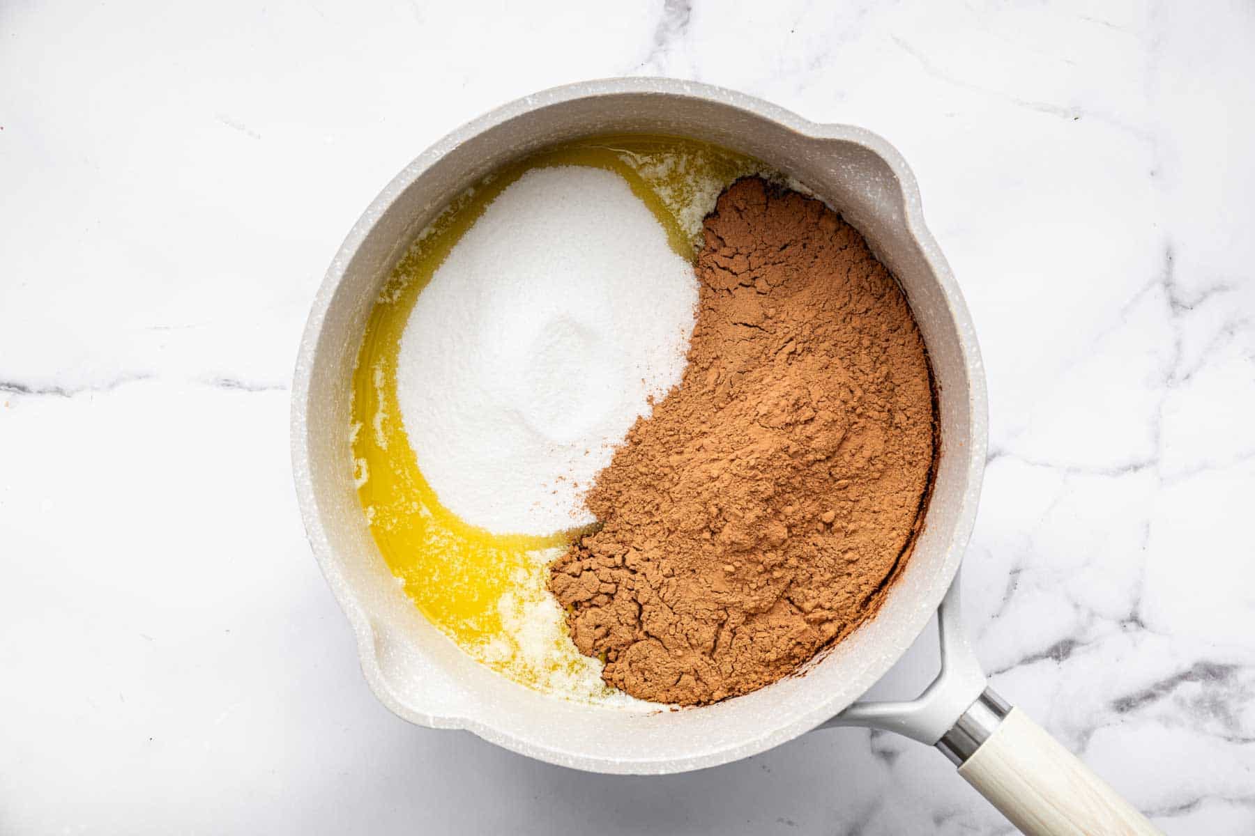 White saucepan with butter, sugar and cocoa powder in it.