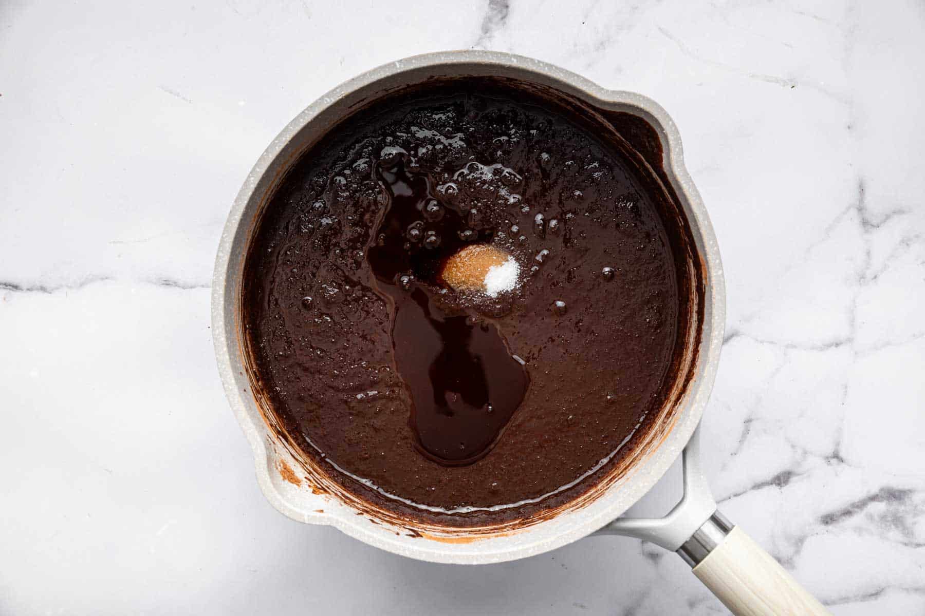 Vanilla and salt being stirred into chocolate mixture in white saucepan.