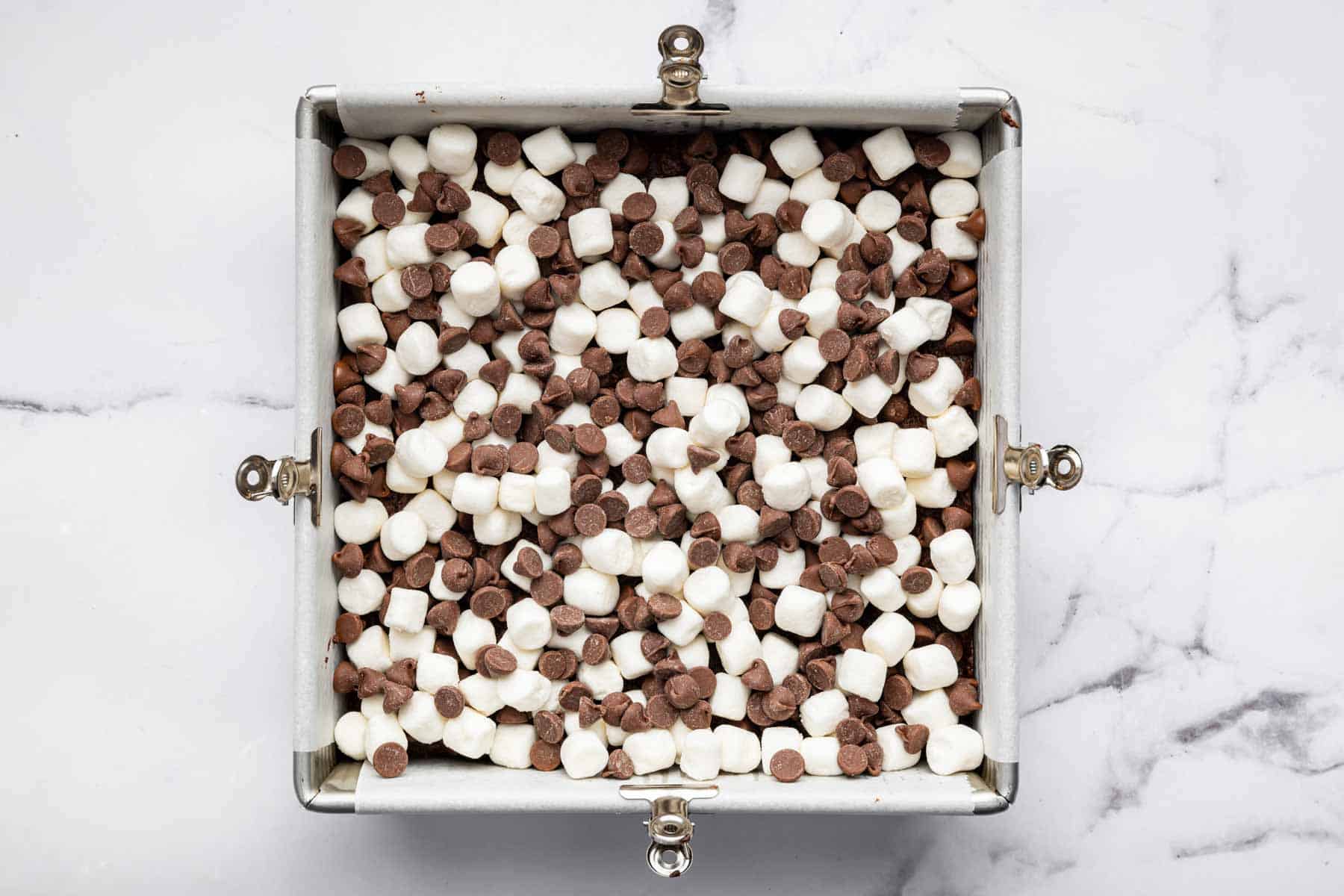 Square baking pan with chocolate chips and white bits on top of everything.