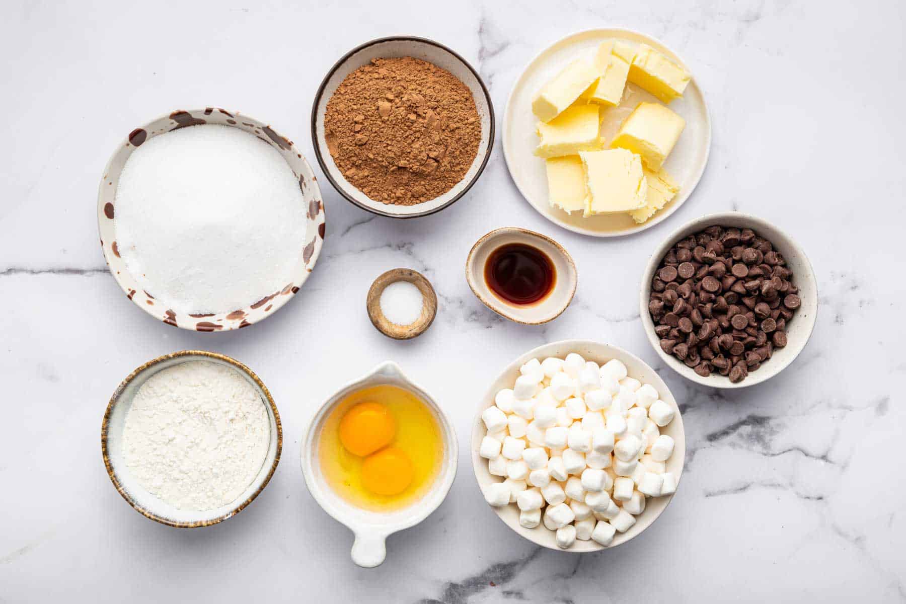 Small bowls with eggs, chocolate chips, cubed butter, and sugars.