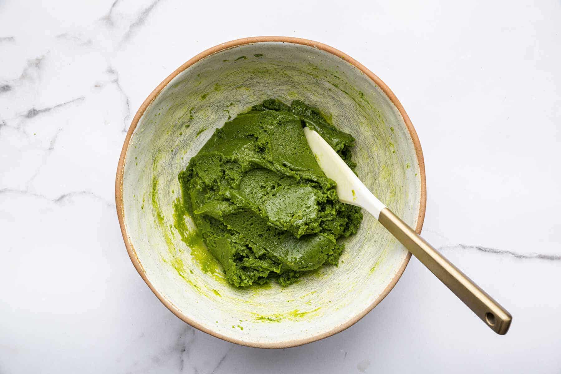 Bright green dough in white bowl with white spatula.