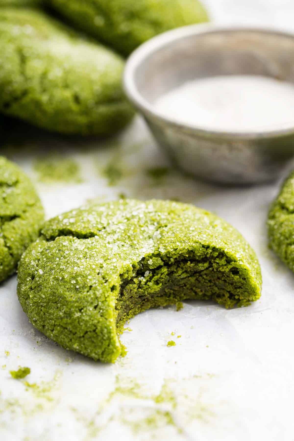 Green dessert with bite missing on white table next to bowl of sugar.