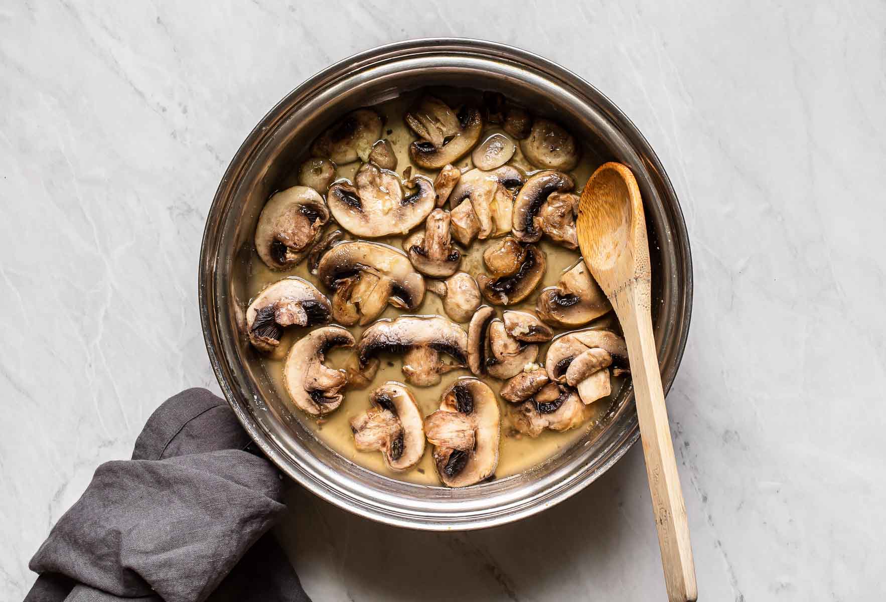 Mushrooms cooking in wine in skillet.
