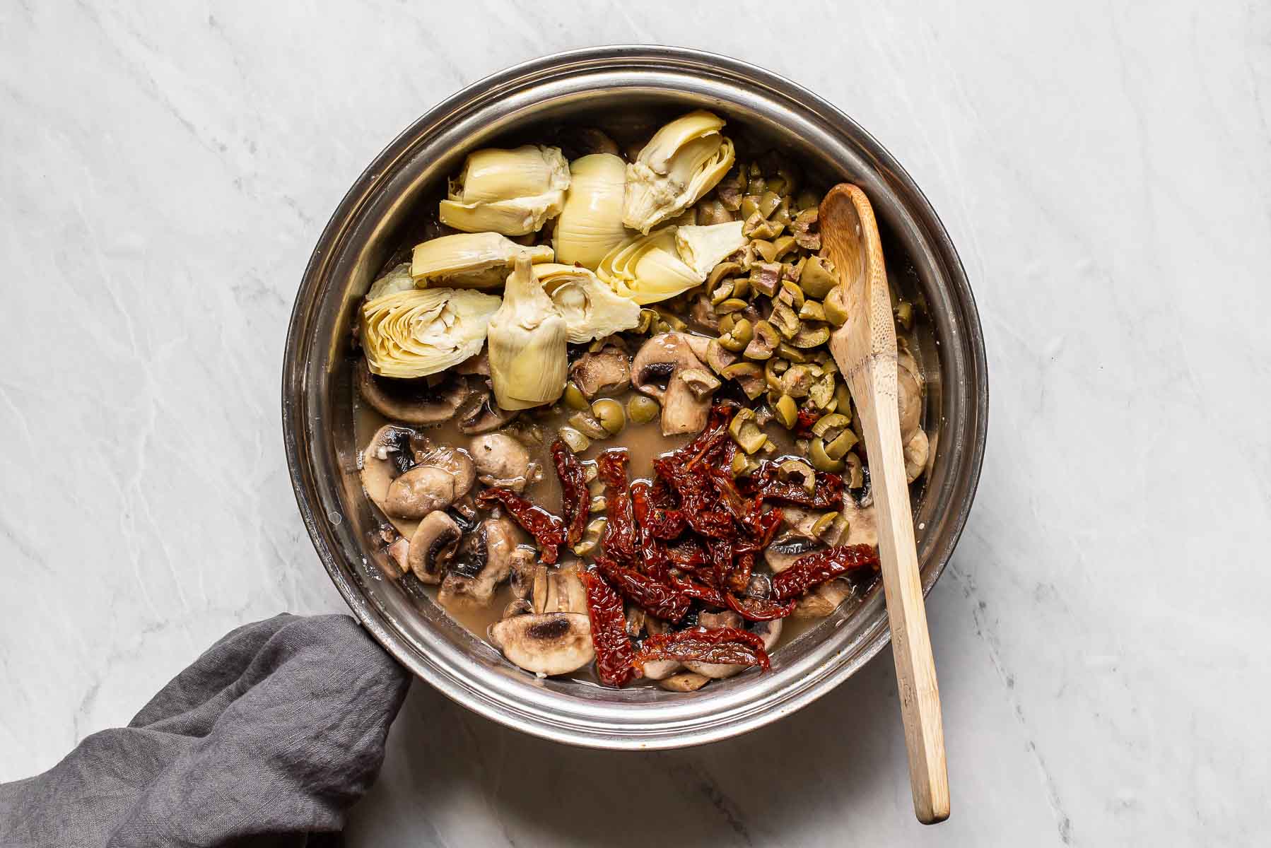 Artichokes, olive, mushrooms, and sun-dried tomatoes in skillet.