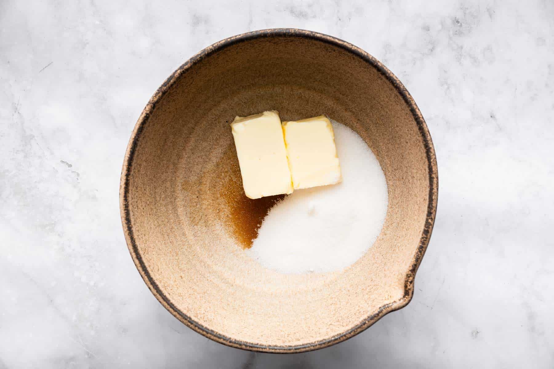 Brown bowl with two butter cubes, sugar and vanilla in it, before beating.