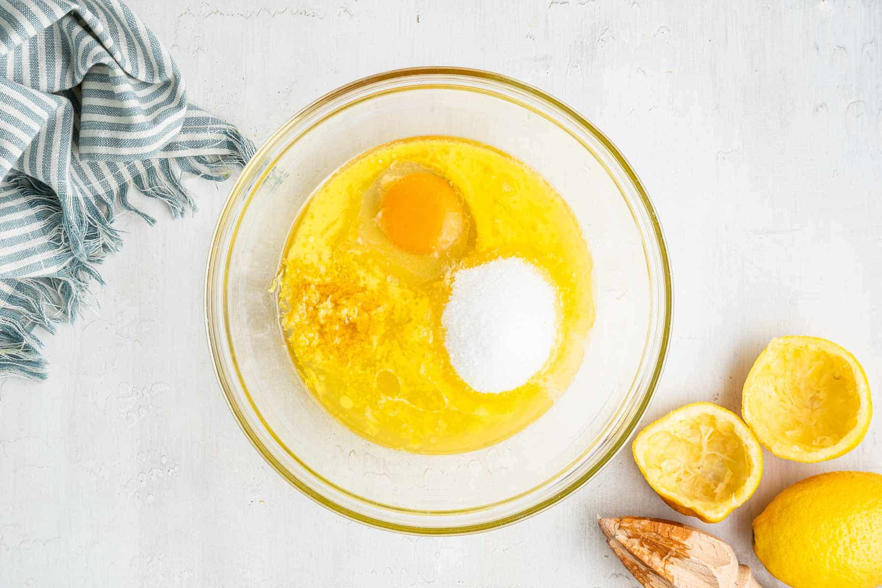 Clear bowl with melted butter, lemon juice, egg and sugar on counter.