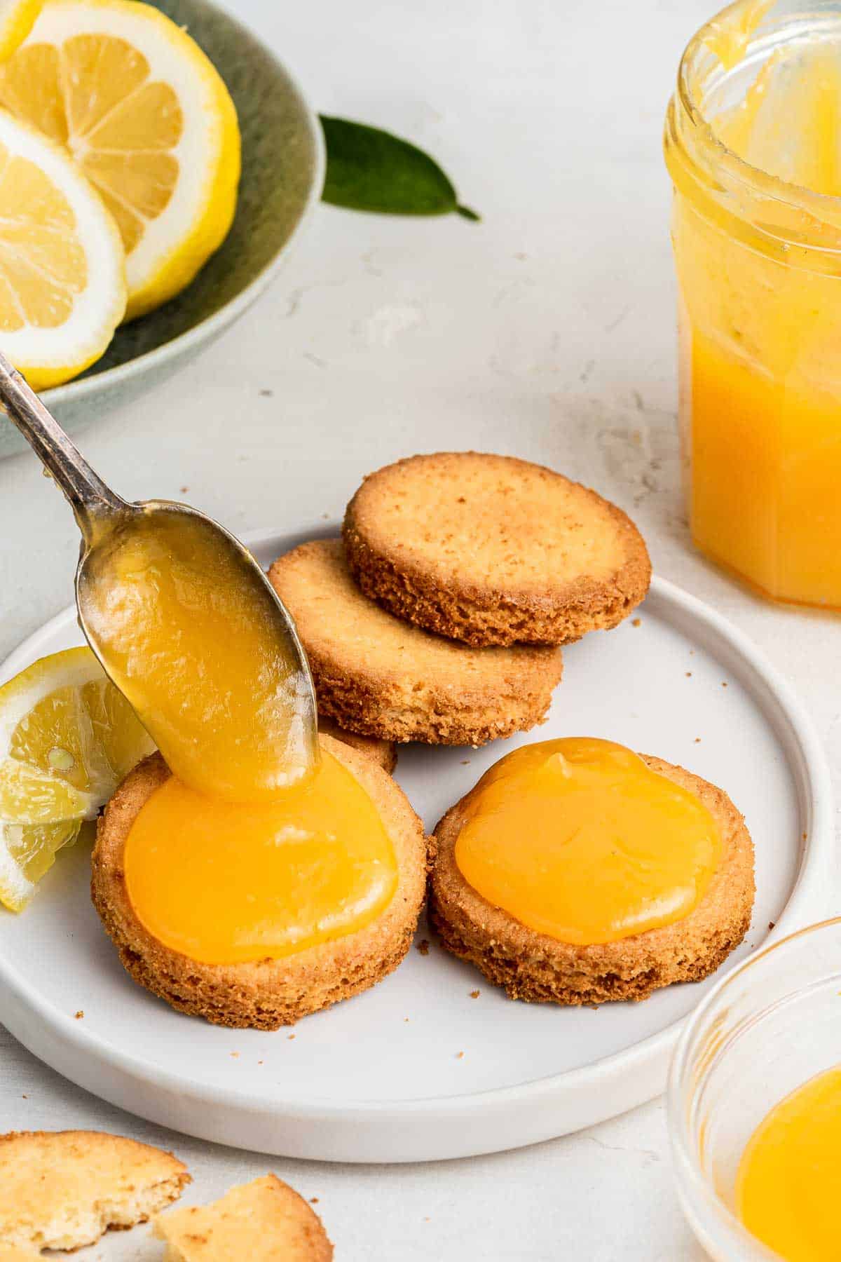 Spooning microwave lemon curd on shortbread cookies with spoon.