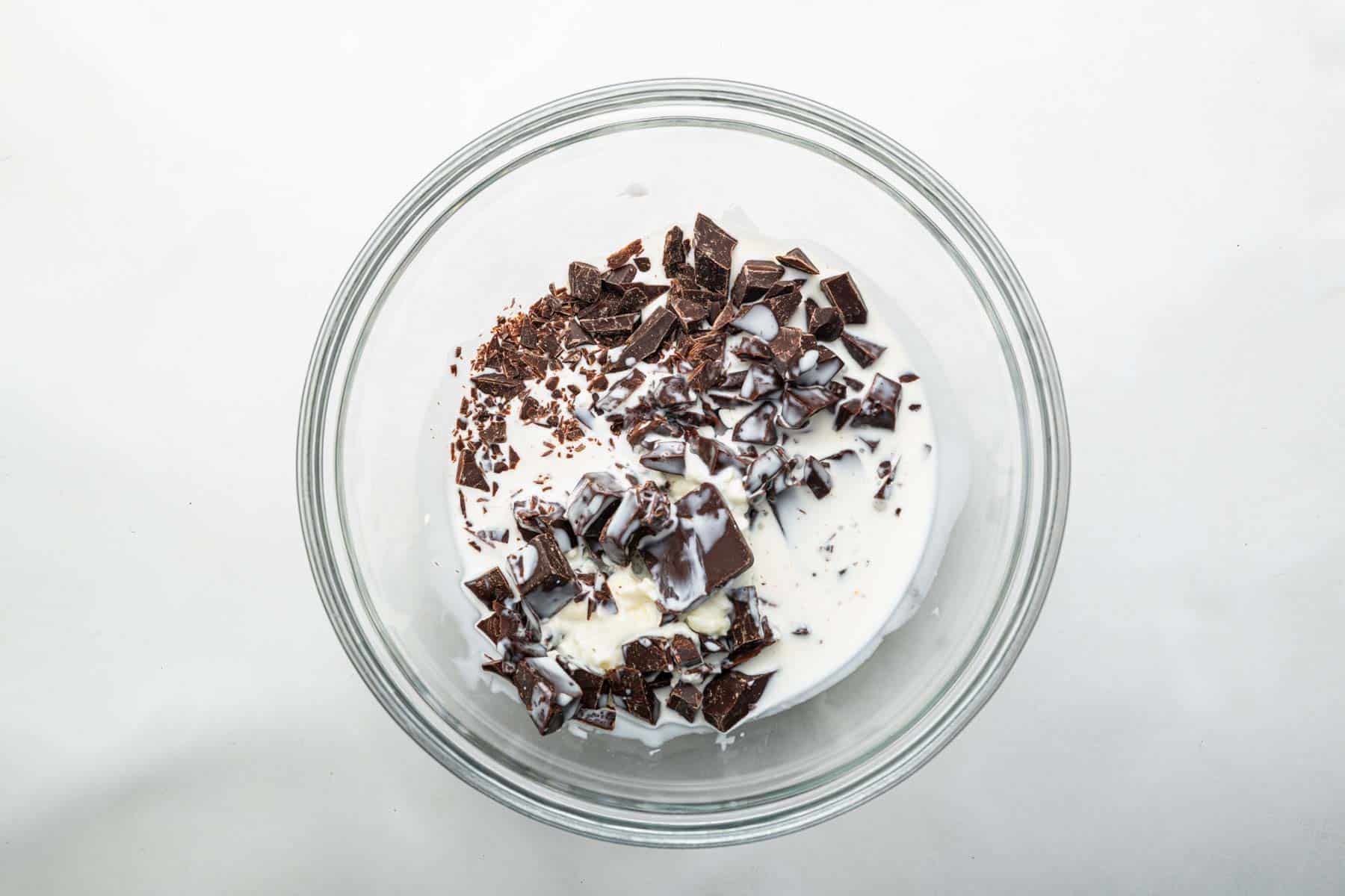 Chopped chocolate and heavy cream in a clear bowl.