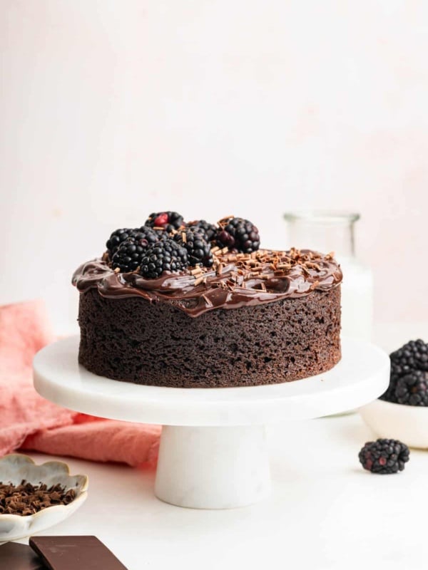 Mini chocolate cake decorated with blackberries on a small white cake stand.