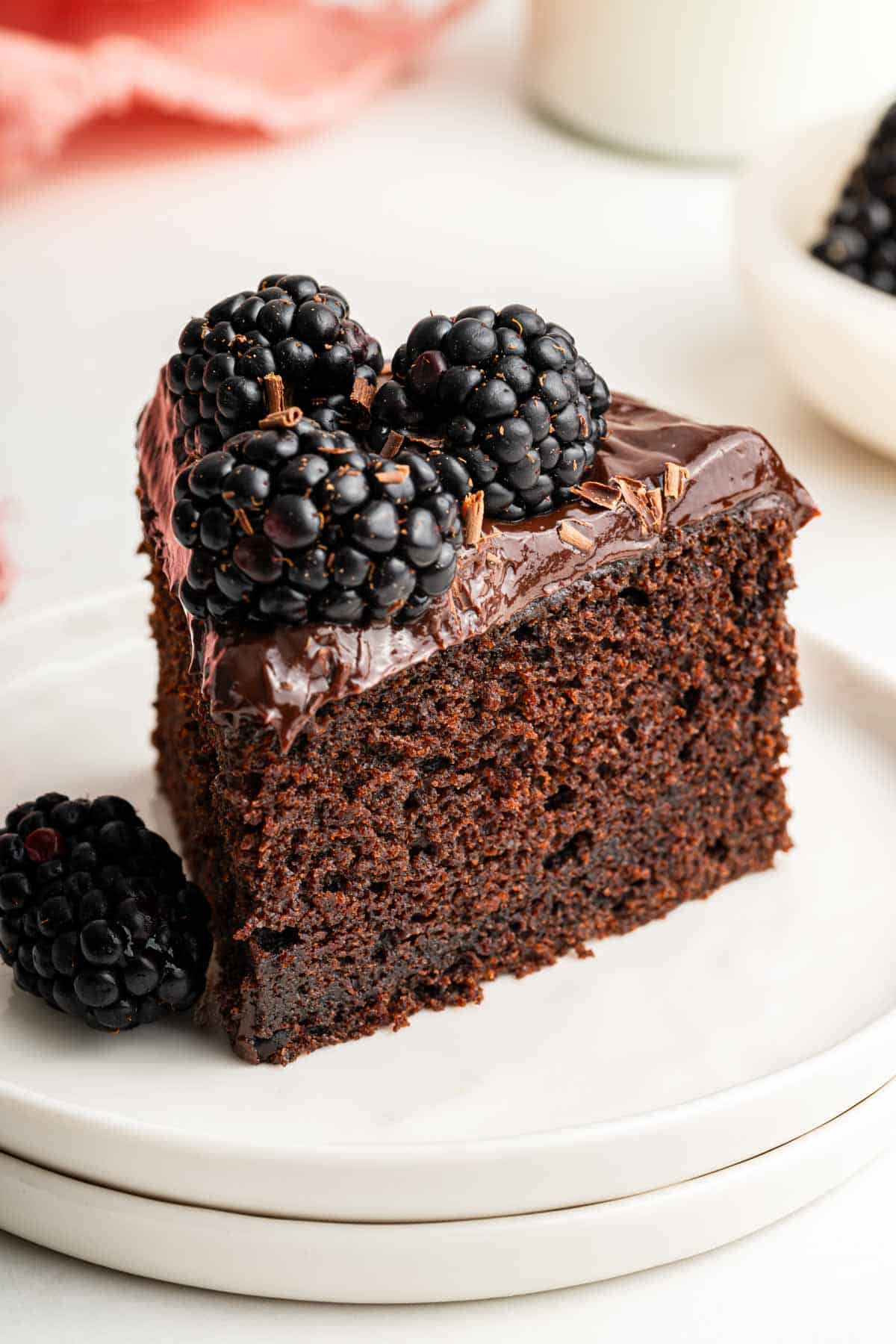 Small slice of chocolate cake on plate with blackberries on top.