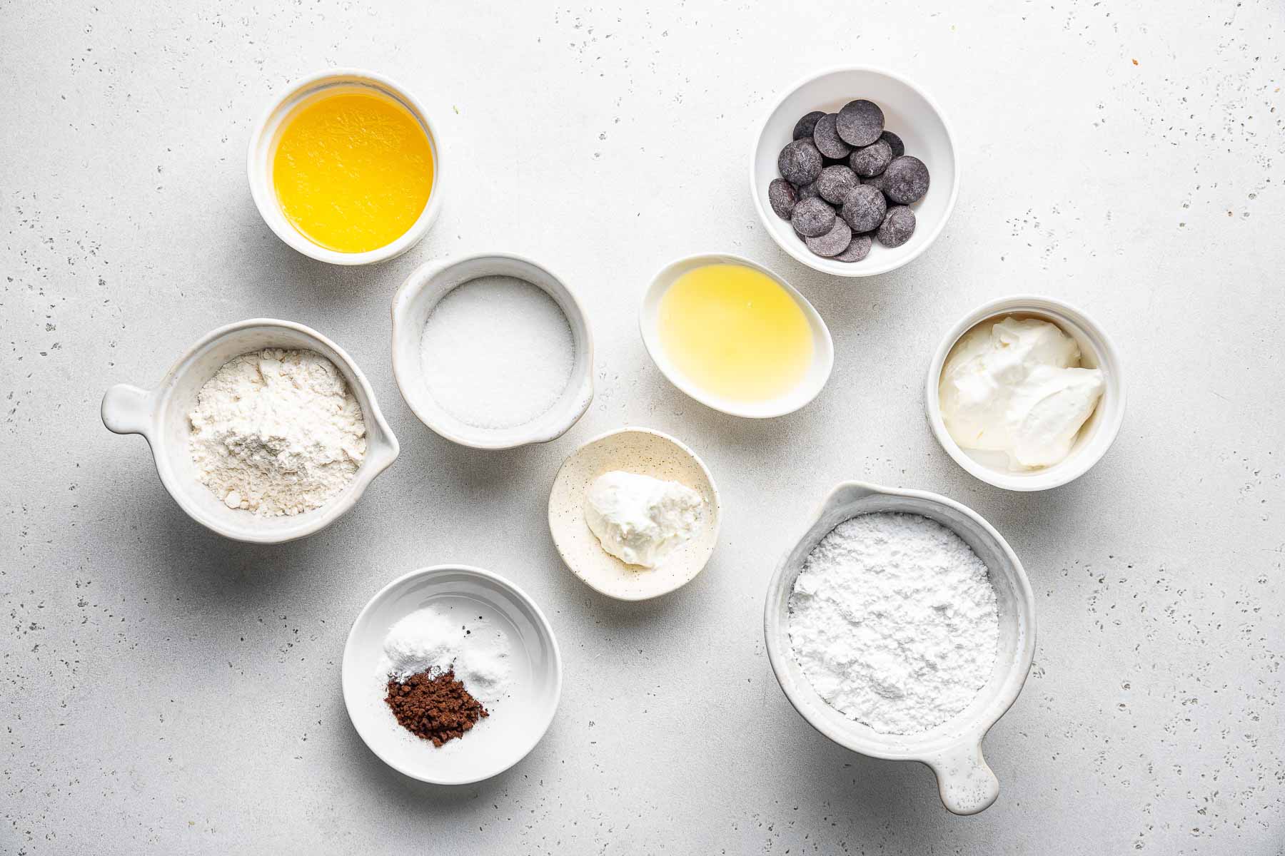 Ingredients for mocha cupcakes in small bowls on white surface.