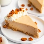 A slice of no bake peanut butter pie on white plate garnished with whipped cream and peanuts.