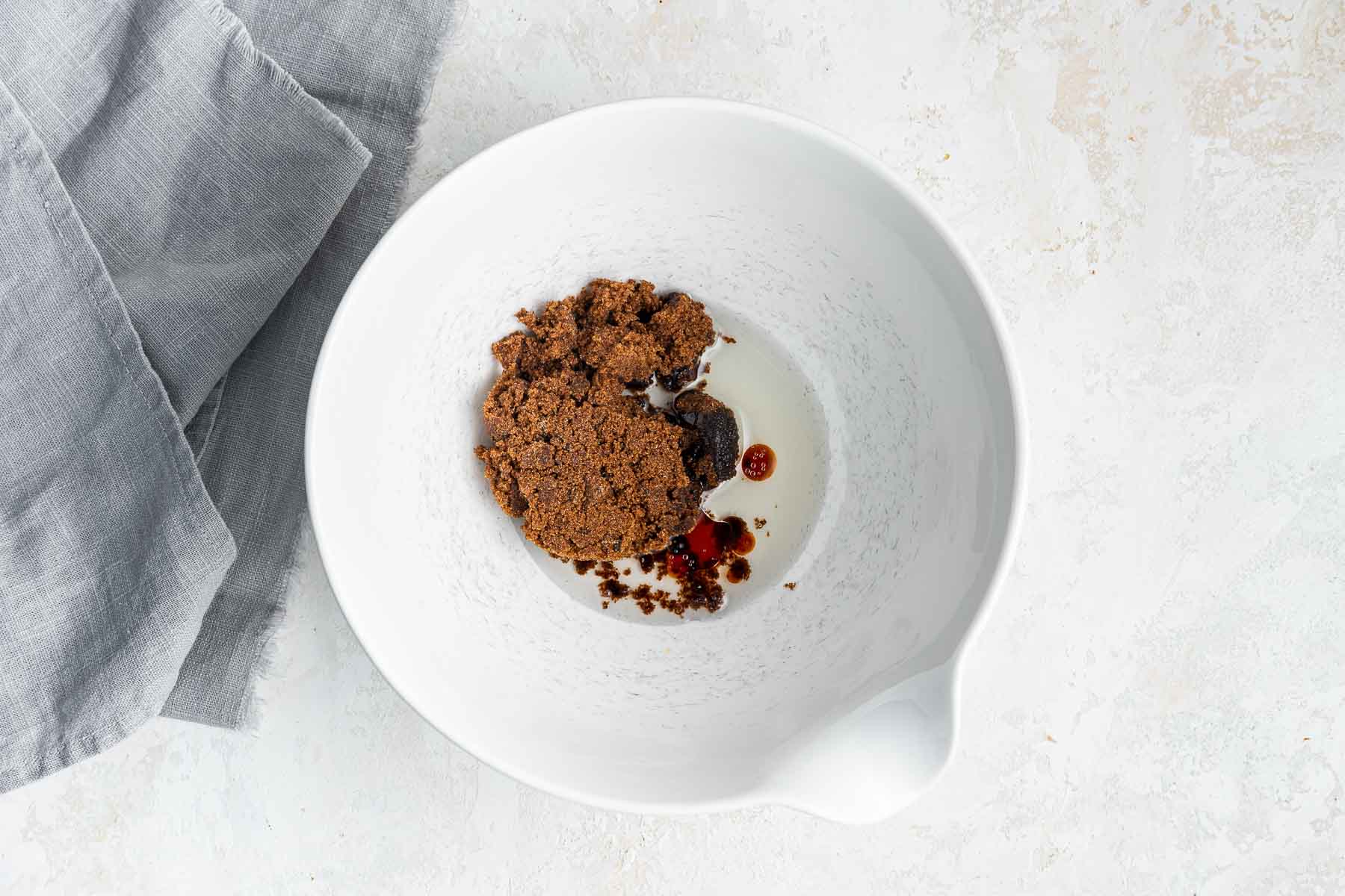 White bowl with oil, vanilla and brown sugar.