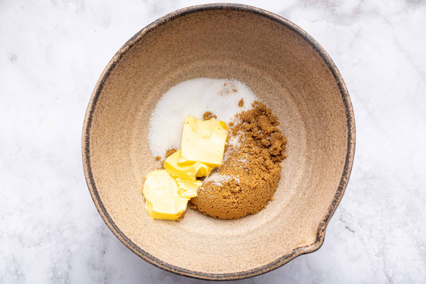 Brown bowl with butter, white sugar, and brown sugar, unbeaten.