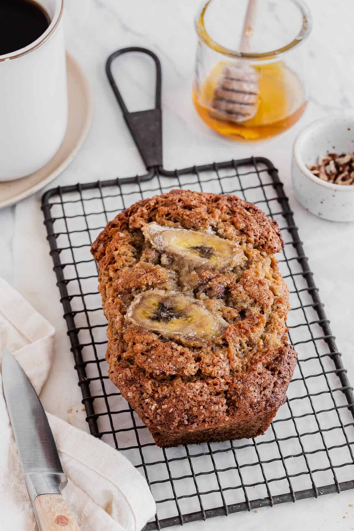 One banana bread loaf on a wire tray with honey in jar.