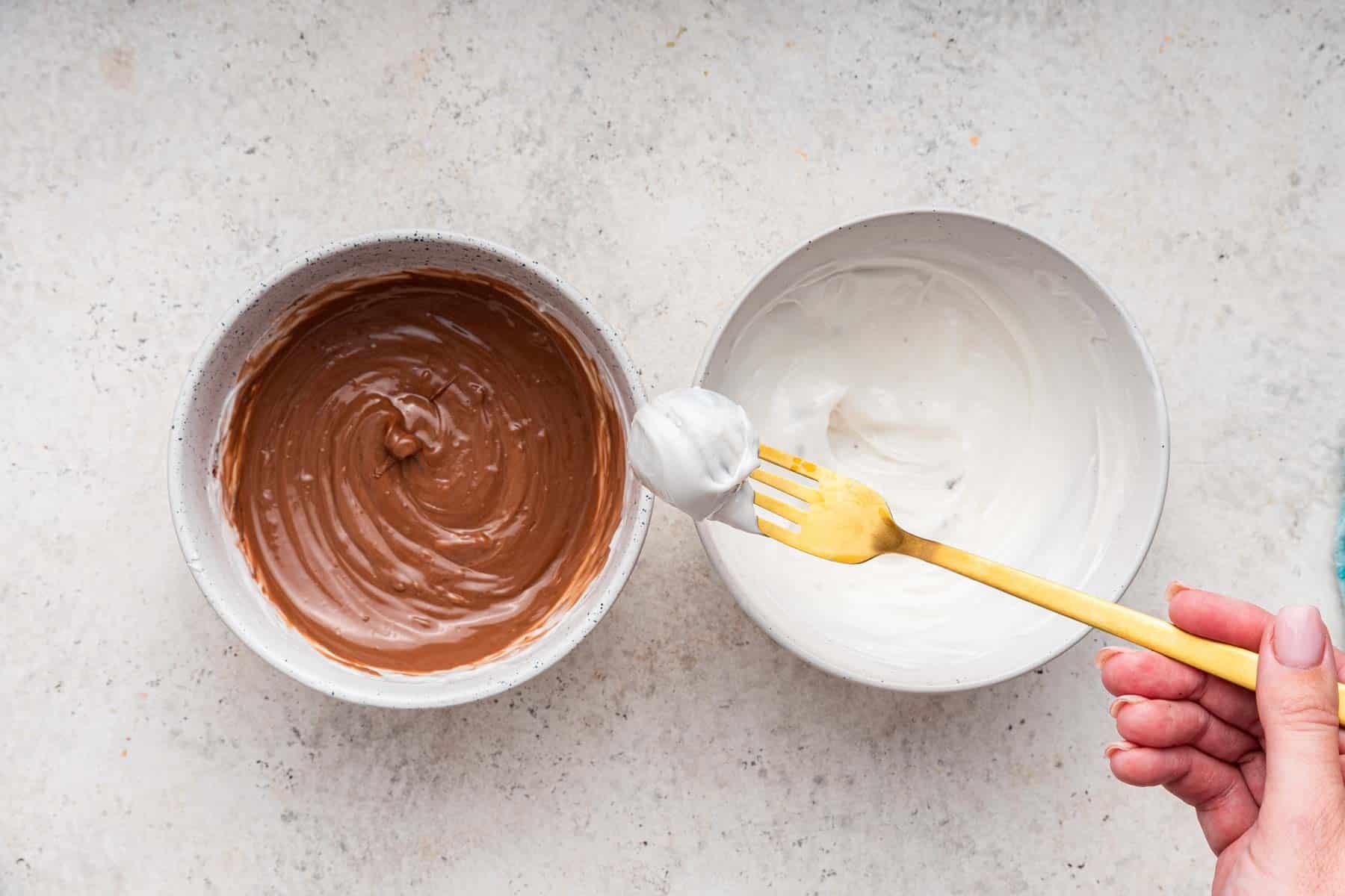 Gold fork dipping a ball in white chocolate over a bowl of brown chocolate.