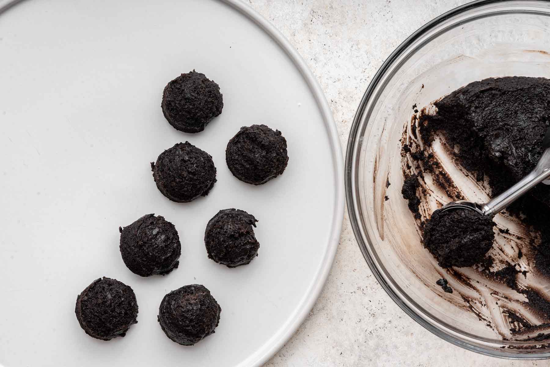 Plate with black balls on it, next to bowl with cookie scoop.