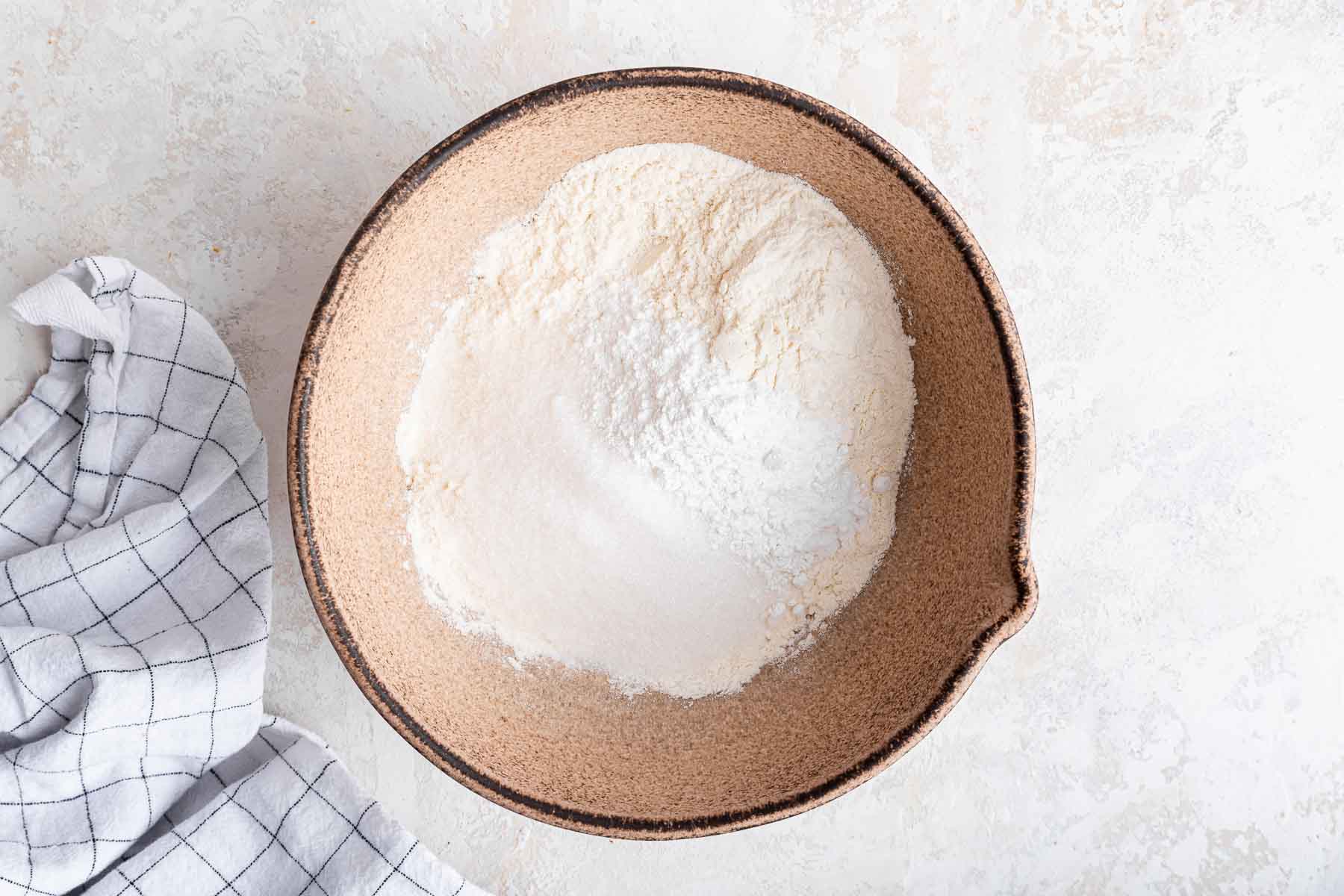 Brown bowl with flour, baking powder and sugar on grey counter.