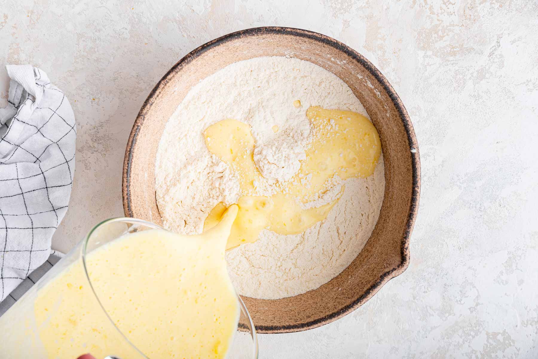 Pouring yellow batter into bowl of flour on grey counter.