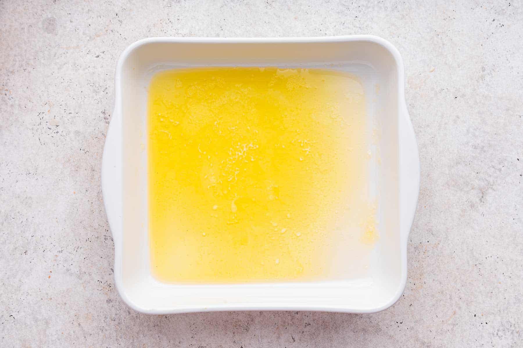 Square white baking dish with melted butter in bottom.