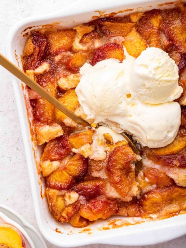 Fresh peach cobbler with scoops of vanilla ice cream on top in a square dish.