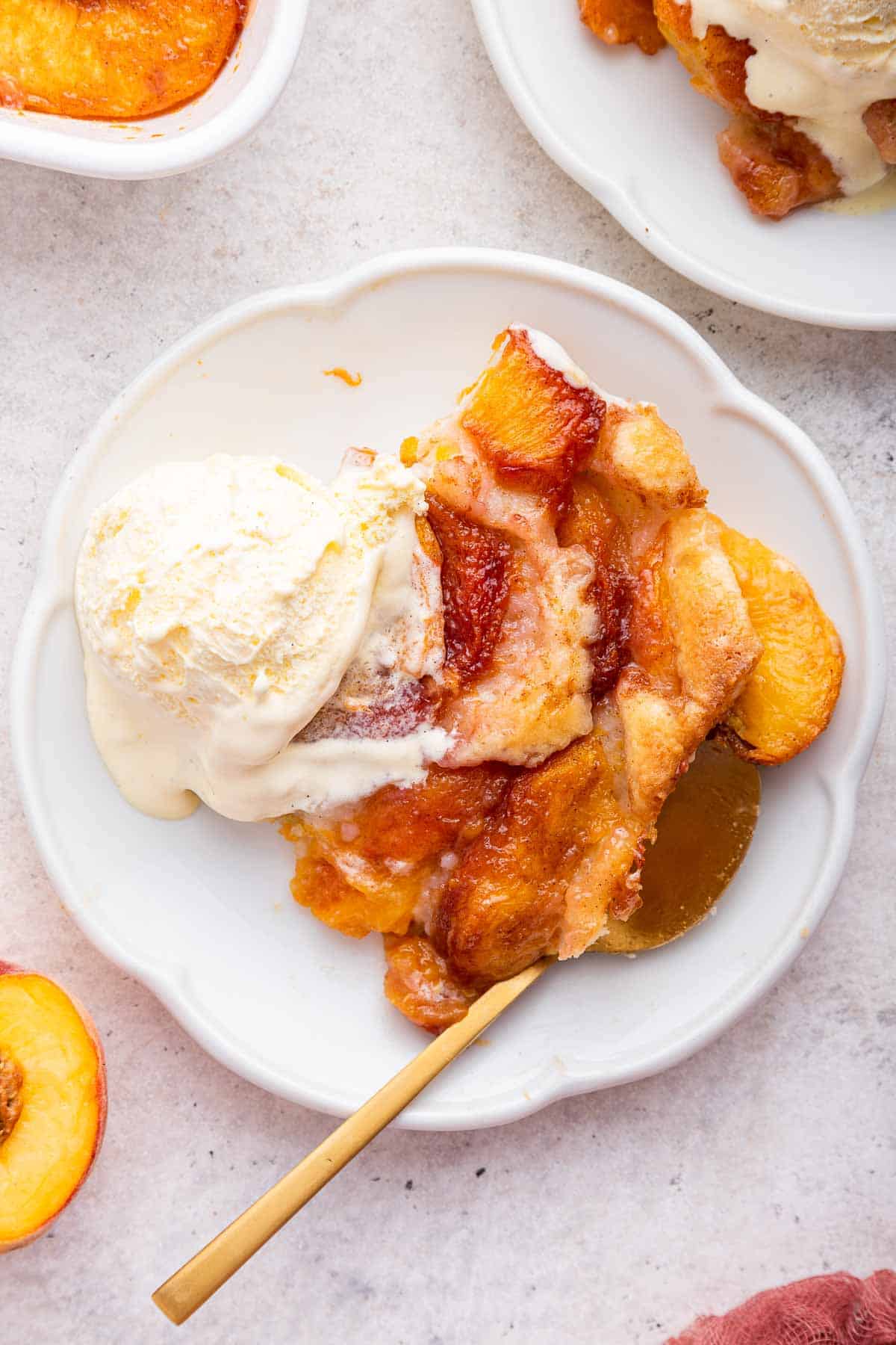 White fluted plate with scoop of fresh peach cobbler and ice cream on top.