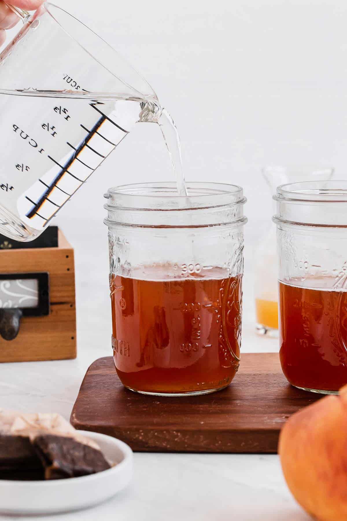 Adding cool water to peach iced tea in mason jars.