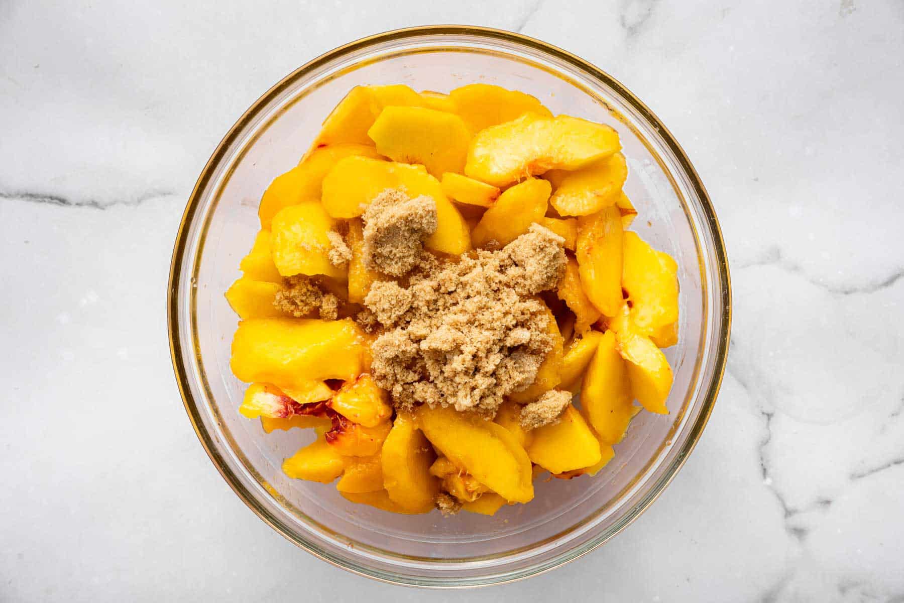 Sliced fruit in bowl with brown sugar sprinkled on top.
