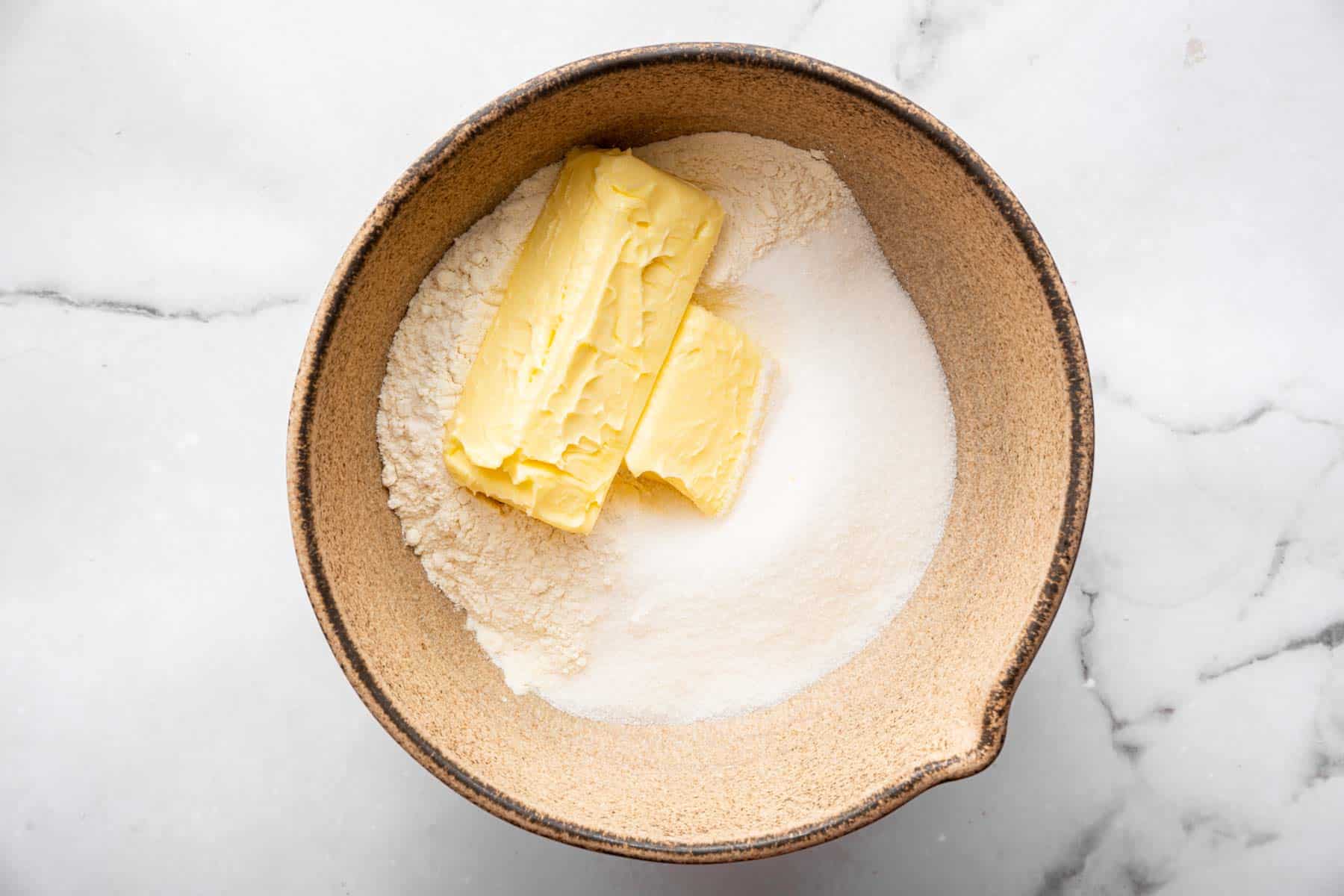 Brown bowl with sticks of butter, sugar, and flour inside.