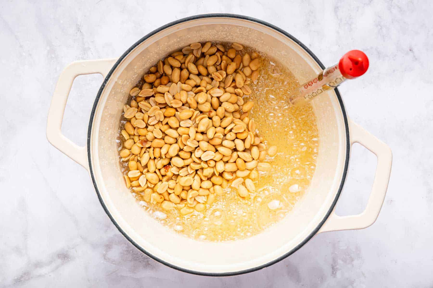 Adding nuts into a pot of light caramel sauce with thermometer on side of pan.