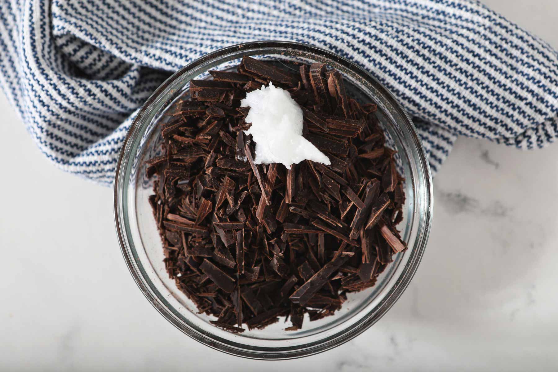 Chopped dark chocolate and coconut oil in glass bowl.